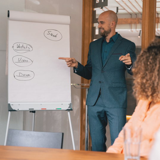 An image of a man standing in front of a whiteboard and pointing to the text written on it. 