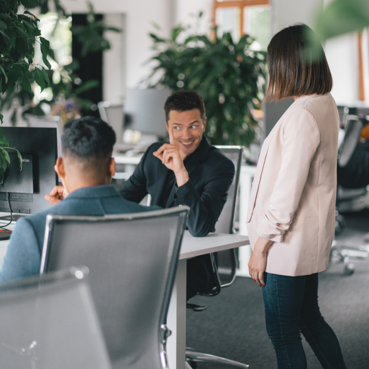 An image of three people having a conversation sitting at a desk.